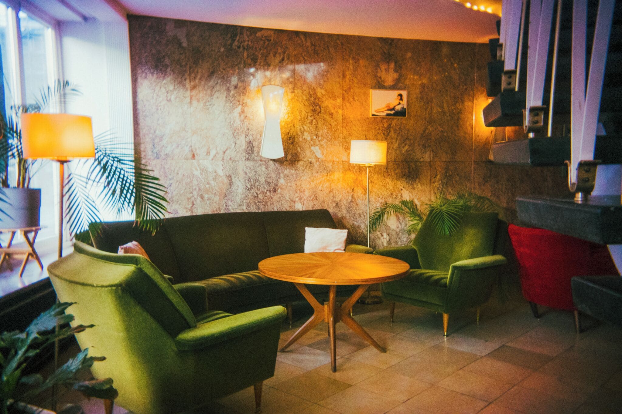 Eine Lobby mit einem grünen Sofa, zwei Sesseln, einem Holztisch und einer Marmorwand mit Wandleuchten.