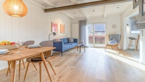 Un vaste espace de vie comprenant une table à manger en bois, un canapé bleu et un luminaire suspendu moderne.