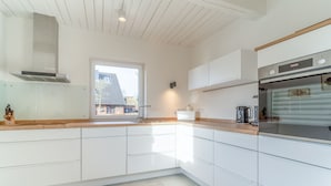 Une cuisine moderne avec des armoires blanches, une hotte de cuisinière en acier inoxydable et un four encastré.