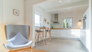 Une cuisine moderne avec des meubles blancs, un coin repas en bois avec deux tabourets et une grande fenêtre qui laisse entrer la lumière naturelle.