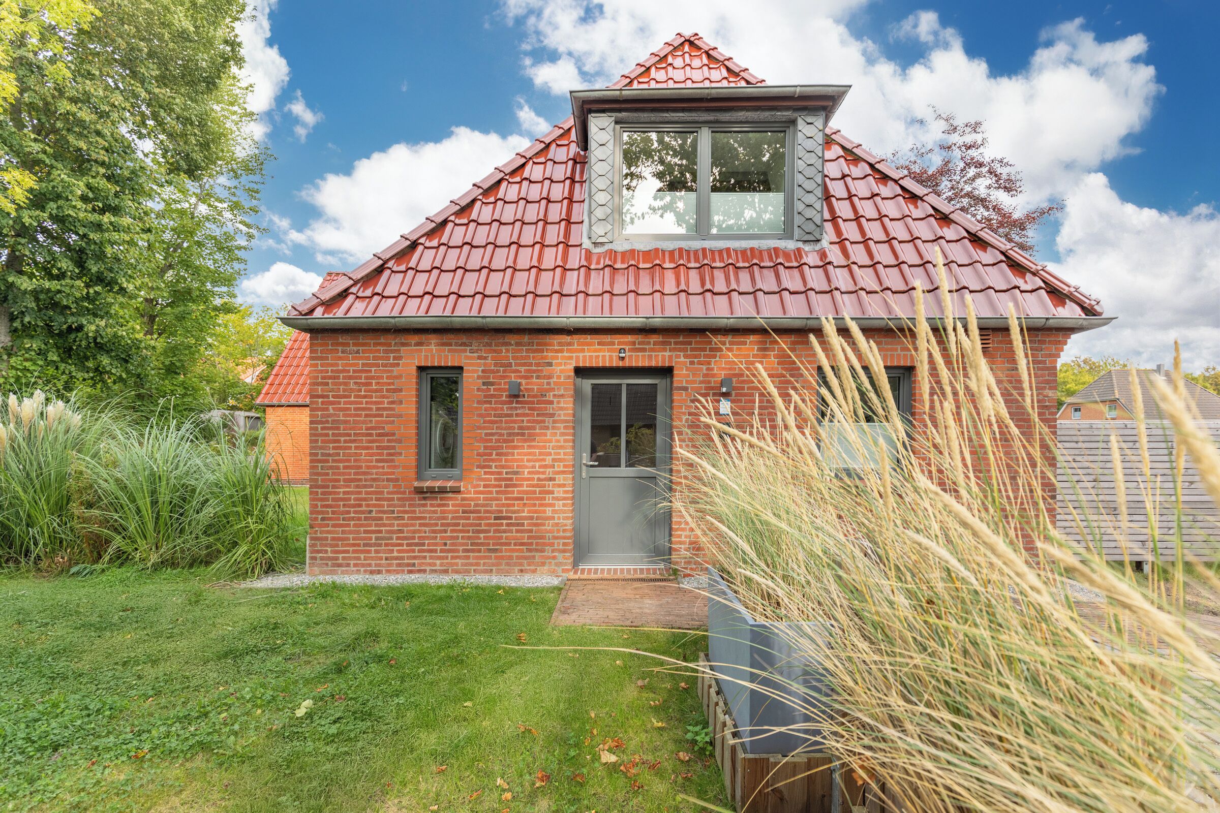 A brick house with a red tiled roof, a small front porch, and a window overlooking the garden.