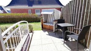 En uteplats med ett bord och stolar i rotting, en träbänk och ett vitt staket.