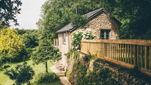 Une maison en pierre avec une clôture en bois, un chemin de jardin et un petit espace extérieur aménagé pour s’asseoir.