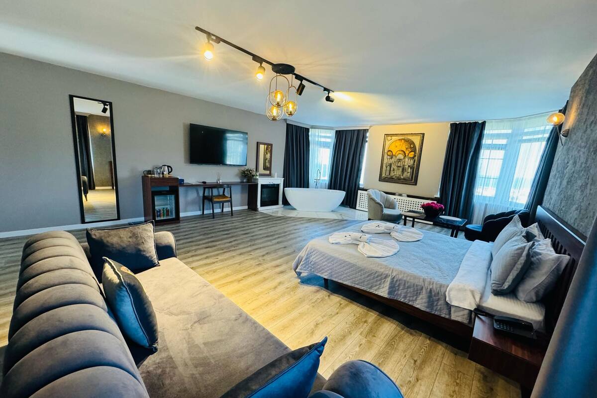 A modern hotel room with a large bed, a sofa, a desk, a flat-screen TV, and a bathroom.