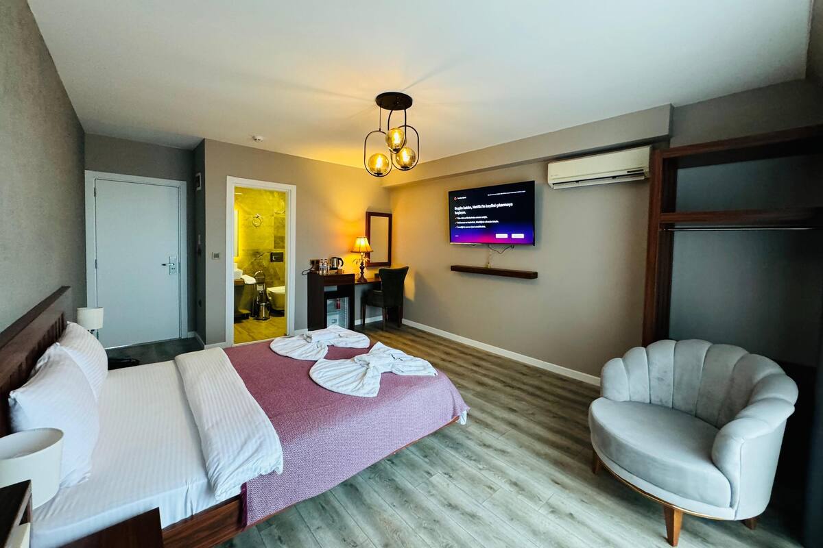 A hotel room with a bed, a desk, a chair, a TV, and a bathroom visible through an open door.
