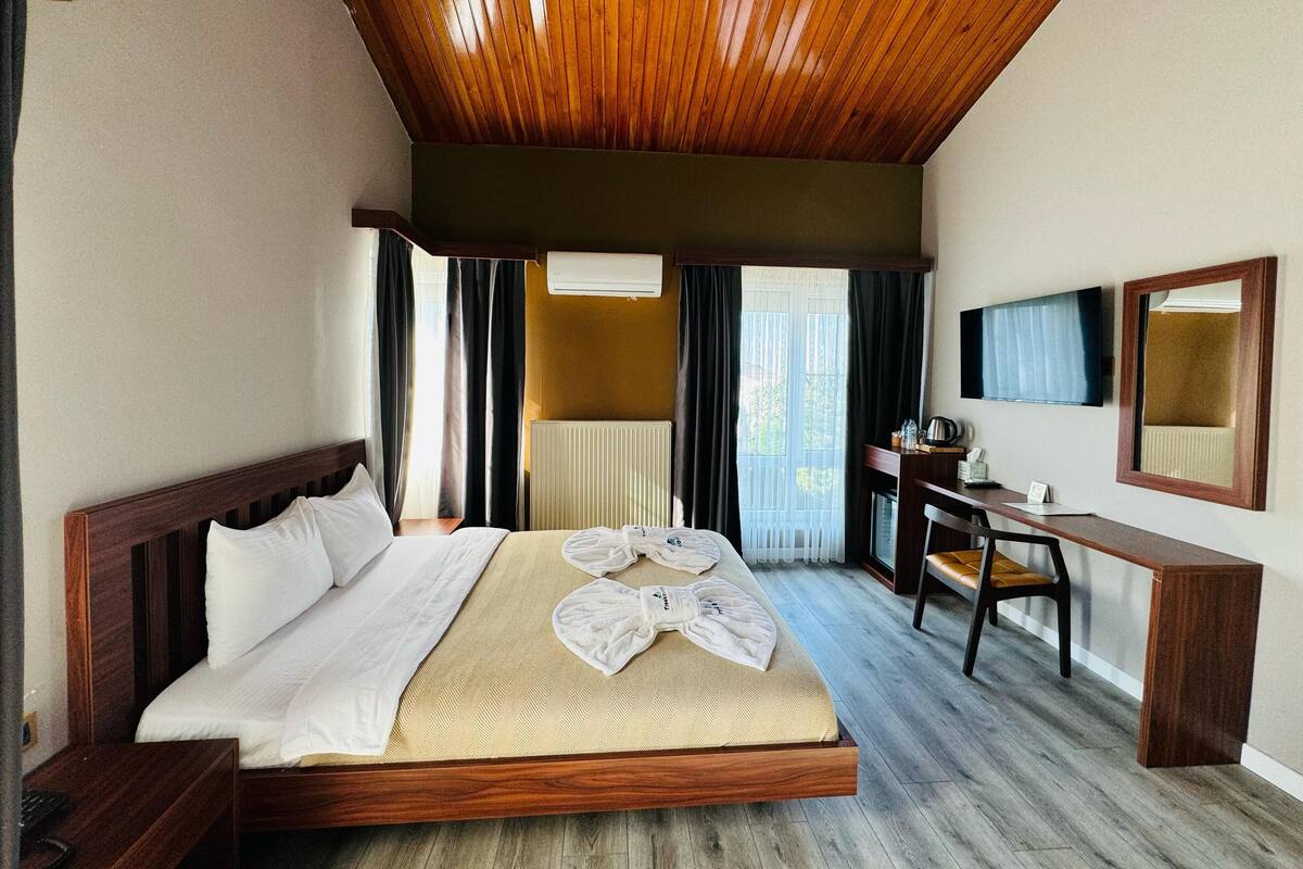A hotel room with a large bed, a desk, a chair, a television, and a mirror.