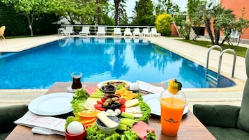 Montaje de comedor junto a la piscina con diversos alimentos y bebidas, incluyendo una ensalada, frutas y una bebida con la etiqueta 'Trekkos Suite'.
