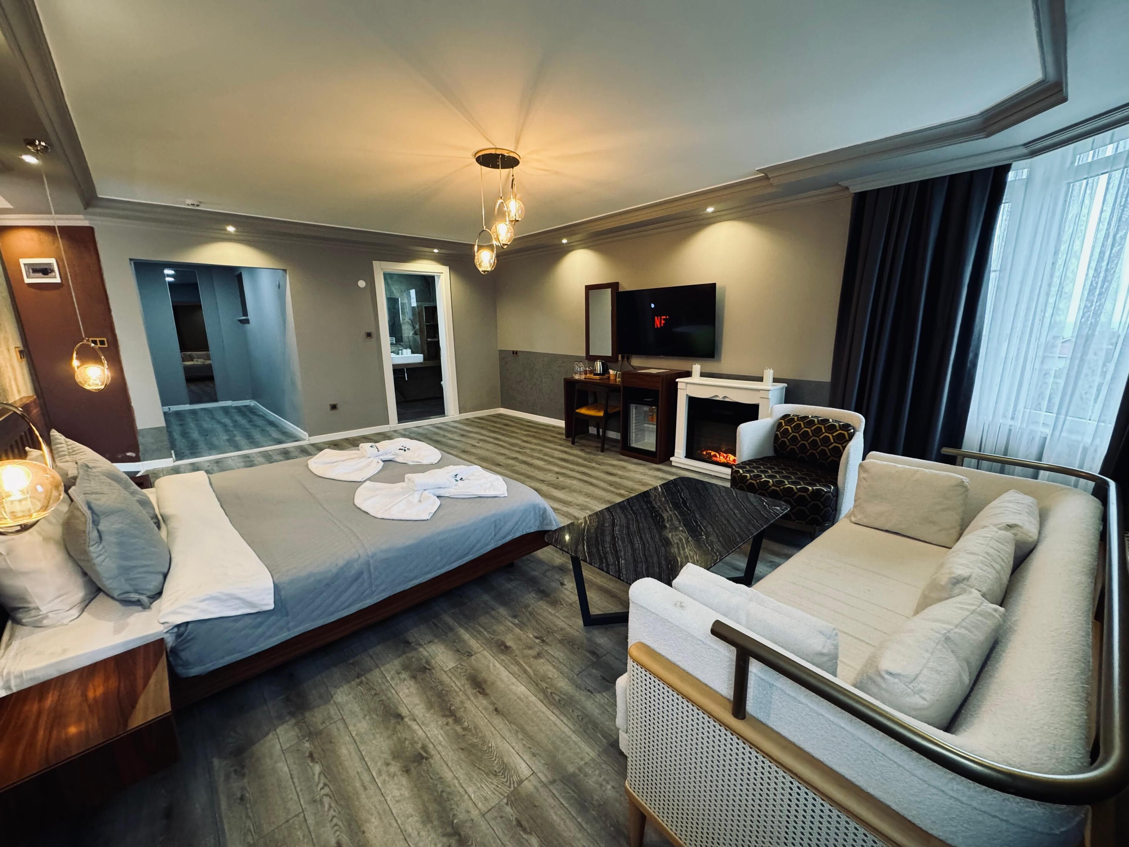 A hotel room with a bed, a sofa, a TV, a fireplace, and a bathroom visible through an open door.