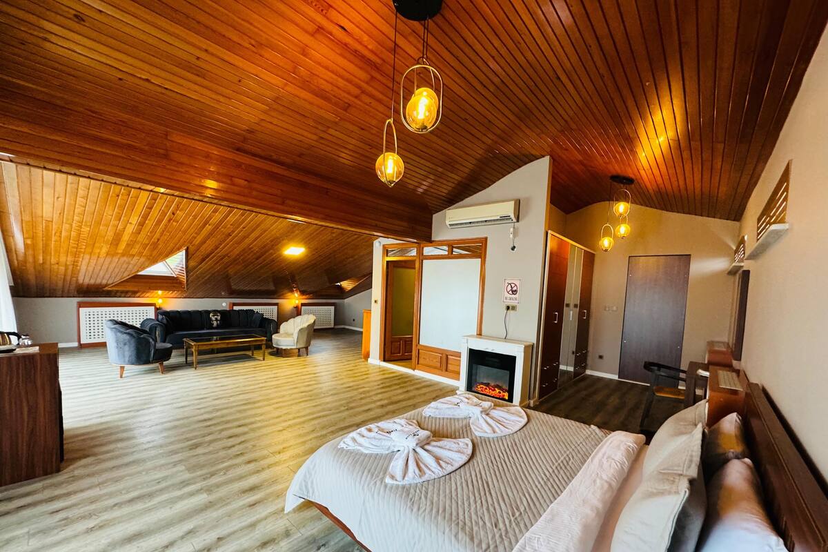 A spacious room with a large bed, a fireplace, a sofa, and a dining table.