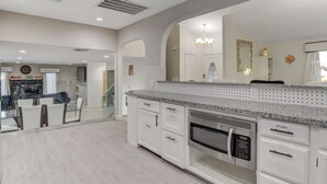 Een moderne keuken met witte kasten, granieten aanrecht, een inbouwmagnetron en een grote spiegel boven de gootsteen.