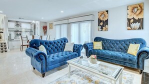 Een moderne woonkamer met twee blauwe banken, een glazen salontafel en een eethoek op de achtergrond.
