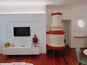 A modern living room with a flat-screen TV mounted on the wall, a white console table with decorative items, a small Christmas tree, and a decorative white and red column.