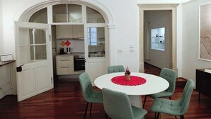 Un espacio habitable compacto con comedor que incluye una mesa redonda y cuatro sillas, una kitchenette con armarios blancos, y un arco que da paso a otra habitación.