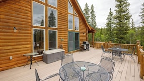 A wooden cabin with a deck featuring outdoor seating and a grill.