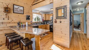 A wooden cabin interior with a kitchen, bar area, and a staircase leading to an upper level.