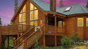 A log cabin with a wooden deck, a staircase, and a chimney.