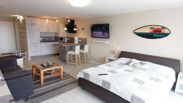 Ett kompakt hotellrum med en säng, en liten sittgrupp, ett litet pentry och en tv på väggen.