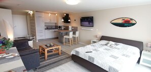 A compact hotel room with a bed, a small sitting area, a kitchenette, and a TV on the wall. - App. Nordstern, Hanseatenhaus Whg. 21 (Sylt)