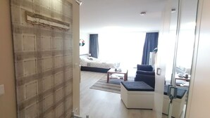 Ett modernt hotellrum med en stor säng, en sittgrupp med soffa och pall, ett litet bord och ett fönster med gardiner.