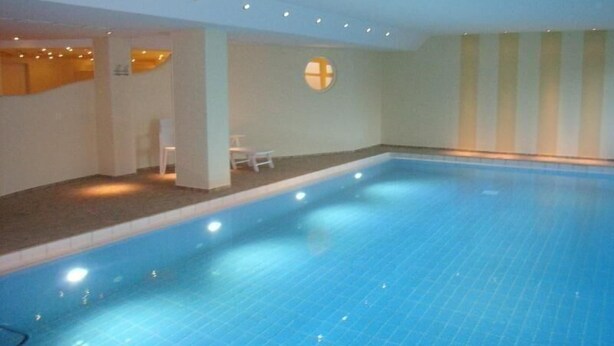 An indoor swimming pool with clear blue water, white walls, and a ceiling with recessed lighting. - App. Stadtoase, Haus Nordland (Sylt)