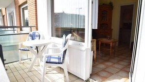 A balcony with a table and chairs, a view of the outside, and a wooden cabinet. - App. Stadtoase, Haus Nordland (Sylt)