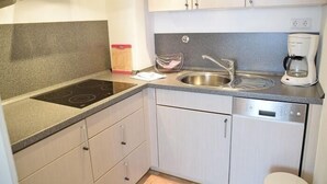 A modern kitchen with a built-in stove, stainless steel sink, and a dishwasher. - App. Stadtoase, Haus Nordland (Sylt)