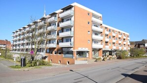A multi-story apartment building with balconies, a visible entrance, and a clear sky. - App. Stadtoase, Haus Nordland (Sylt)