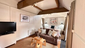 Un salon confortable avec un téléviseur à écran plat, un canapé marron avec des coussins, une table basse en bois et un radiateur.