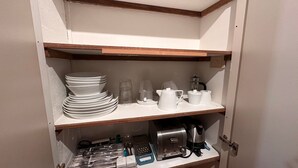 Un garde-manger de cuisine avec des étagères où sont rangées des assiettes, des tasses, une machine à café et des ustensiles.