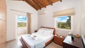 A bedroom with a wooden ceiling, a bed with white bedding, a nightstand, a desk with a plant, and a window with a view of greenery. - Villa Chrysallis (Apokoronas)