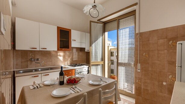 A kitchen with a dining table set for two, a stove, and a window with a view of buildings.