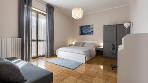A bedroom with a bed, a desk, a chair, a radiator, and a painting on the wall.