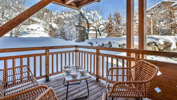 A wooden deck with wicker chairs and a glass table, overlooking a snowy landscape.