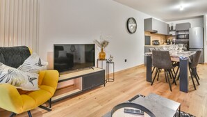A modern living room with a flat-screen TV, a yellow armchair, and a dining area with a table set for four.