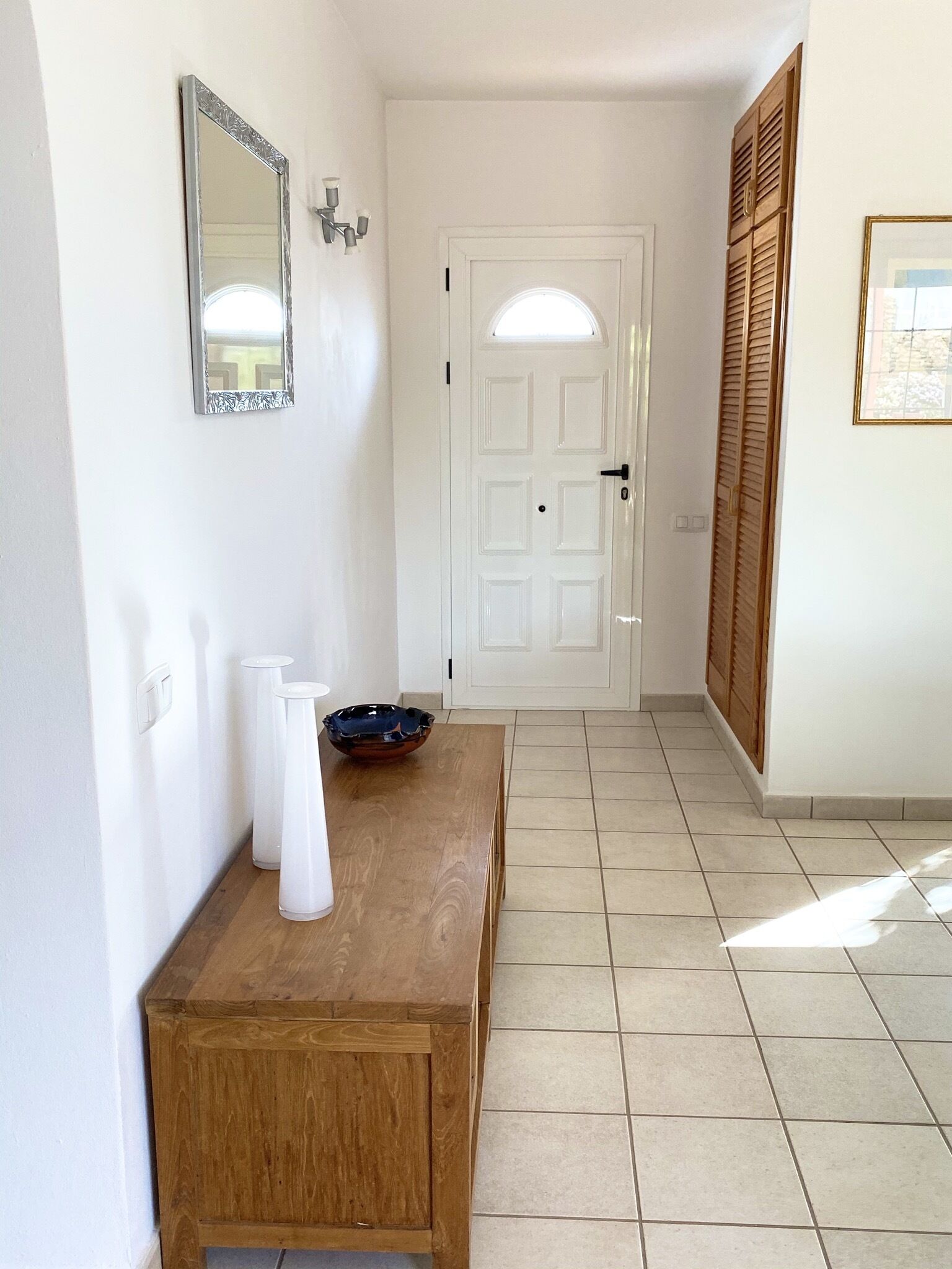 A hallway with a wooden bench, a white door, and a mirror on the wall.
