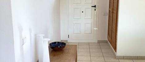 A hallway with a wooden bench, a white door, and a mirror on the wall.