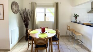 A dining area with a round table, chairs, a vase with branches, and a clock on the wall.