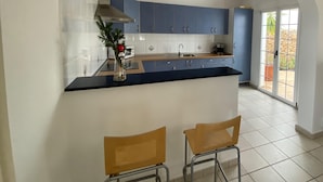 A kitchen with blue cabinets, a black countertop, and two wooden chairs.