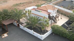 A modern building with a flat roof, surrounded by palm trees and a white fence.
