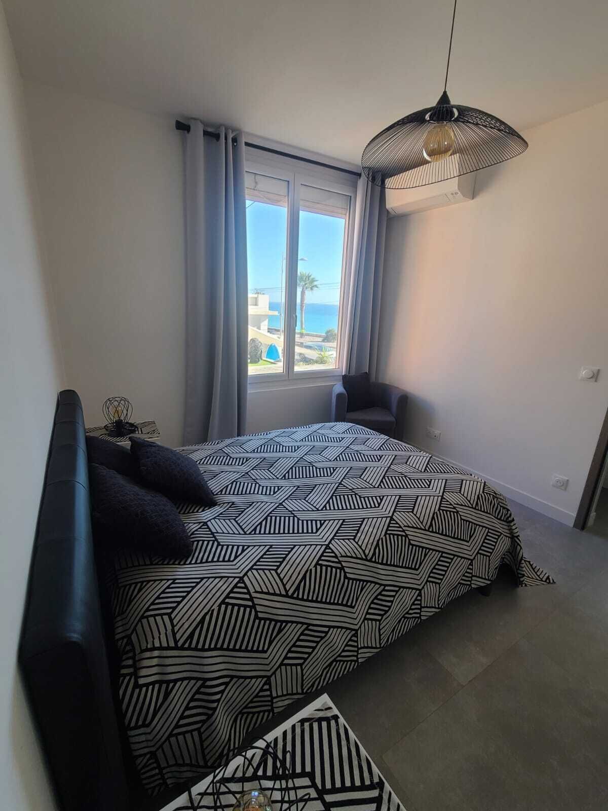 Une chambre à coucher avec un lit, une chaise, une fenêtre avec des rideaux et un luminaire suspendu.