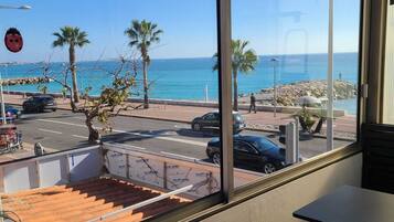 Vista dalla finestra su una spiaggia con palme, una strada e auto parcheggiate.
