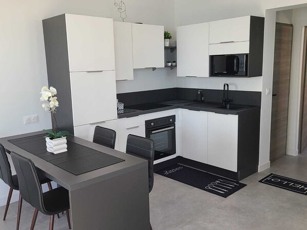 A modern kitchen with white cabinets, a black countertop, a built-in microwave, and a dining area with a table and chairs.
