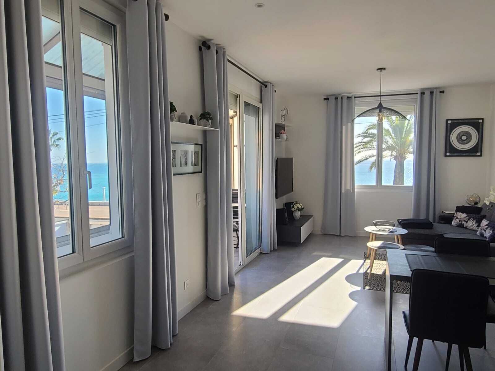 Un soggiorno moderno con zona pranzo, ampie finestre con tende, una televisione a schermo piatto e vista sull'oceano.