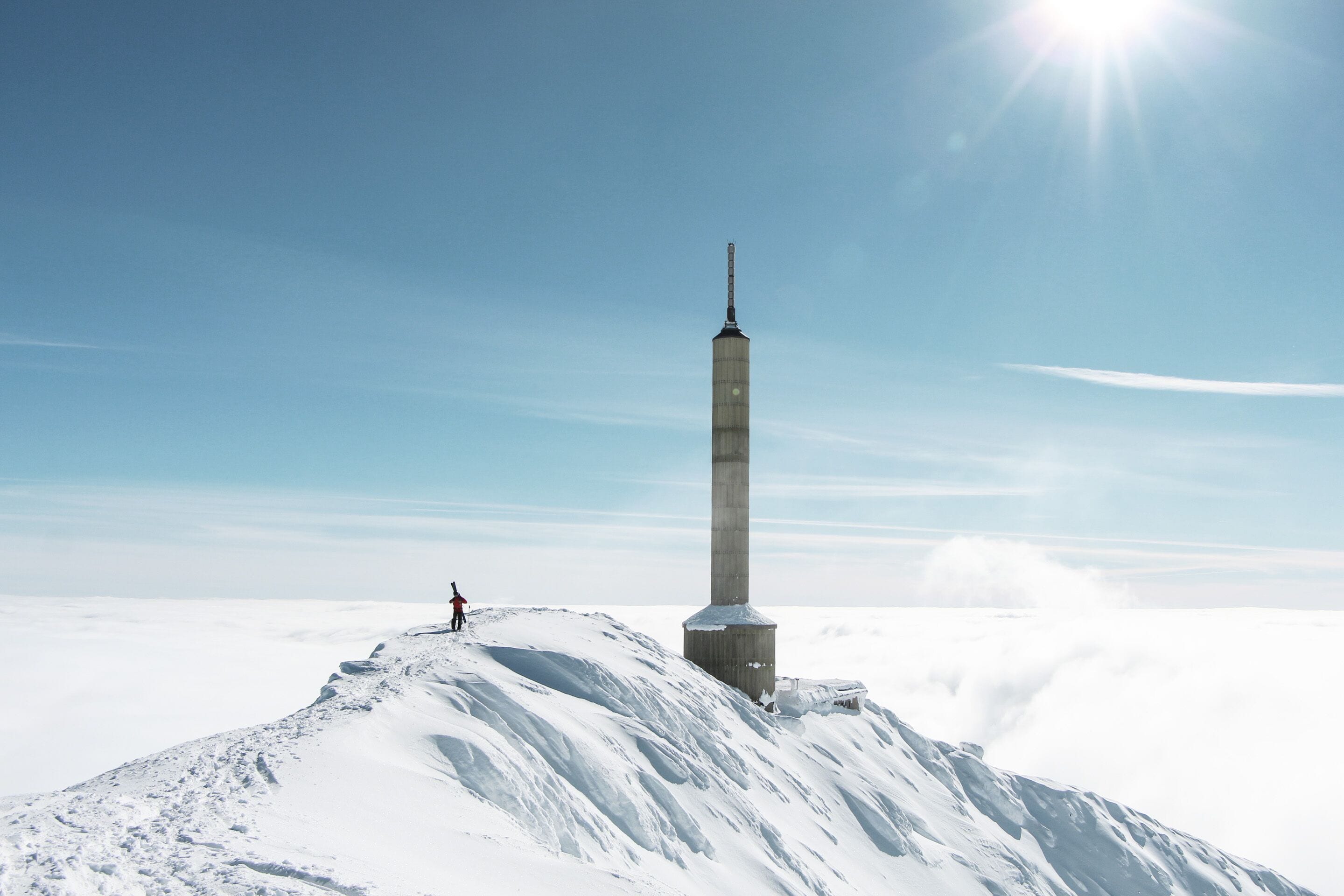 A tall, narrow monument on a snowy peak with a clear sky and sunlight.