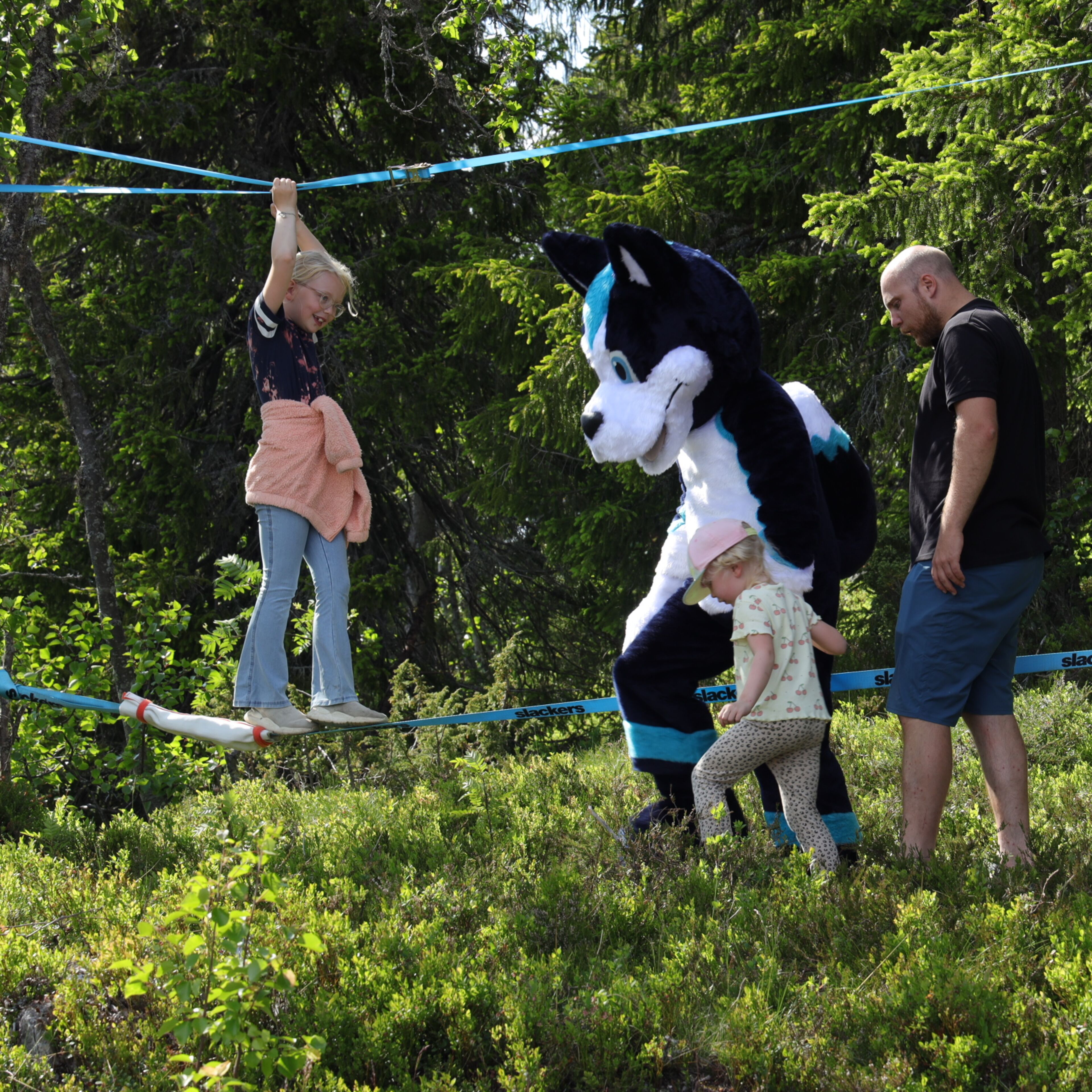 A person in a bear costume on a slackline in a wooded area with trees and greenery.