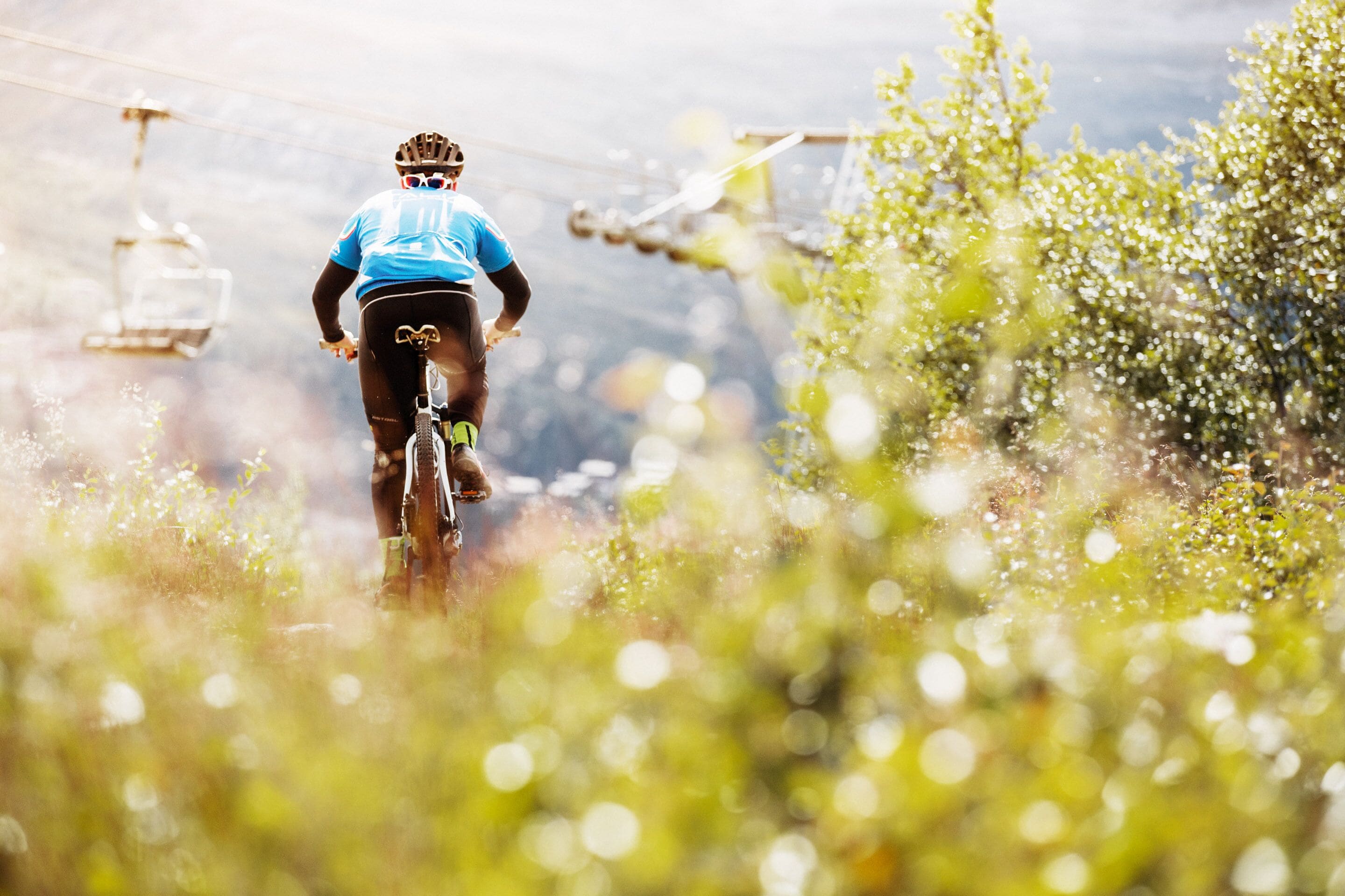 Un ciclista de montaña en un sendero, con un teleférico al fondo.