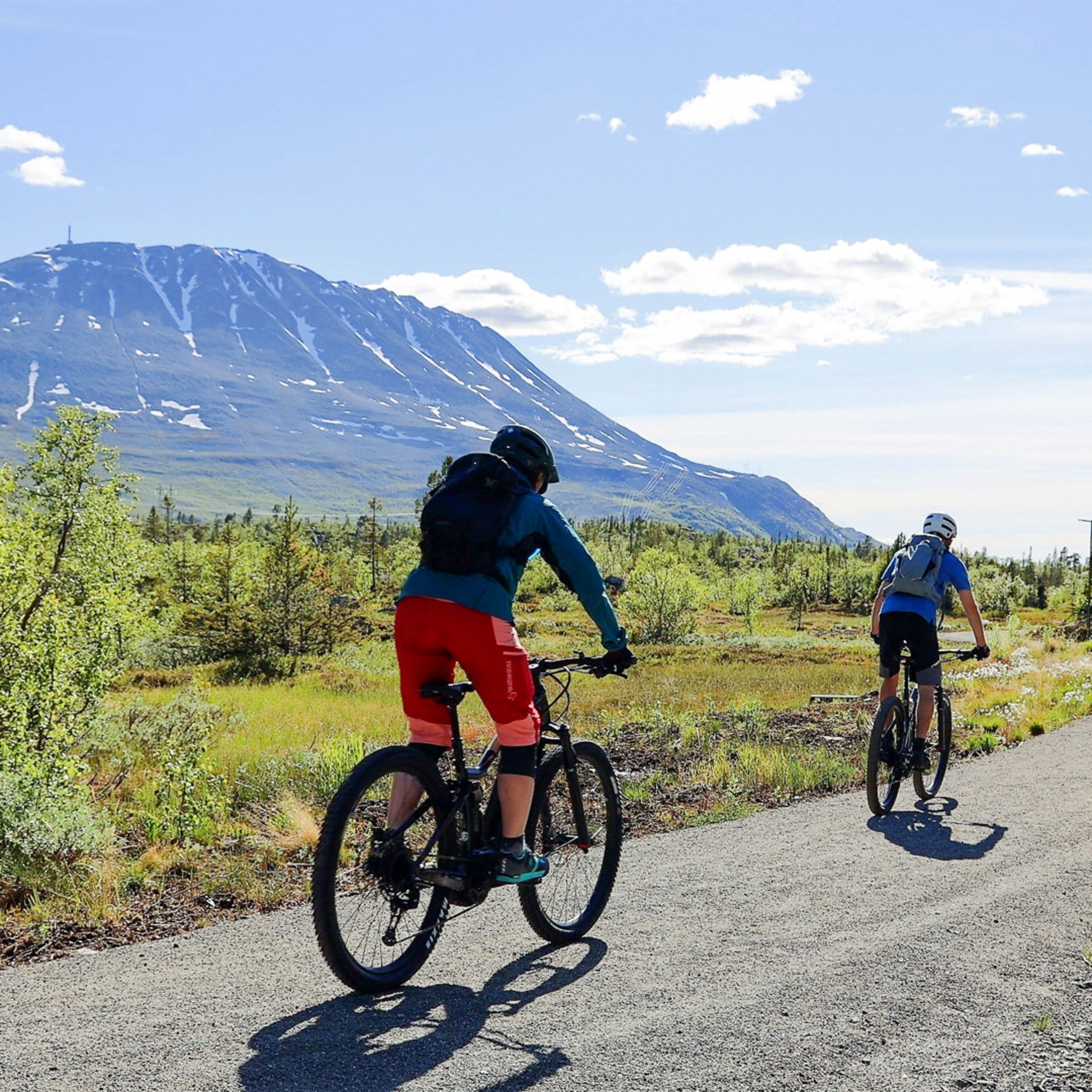 Dos ciclistas en un camino pavimentado, con una montaña al fondo.