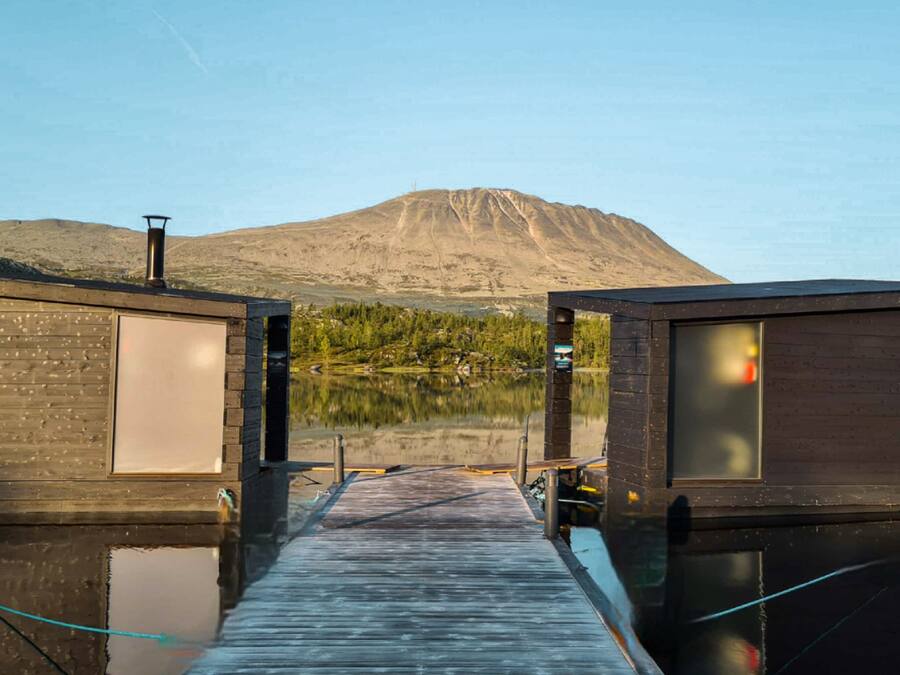 A wooden dock leading to two cabins with a mountain in the background.