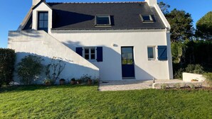 Een huis met twee verdiepingen, een schuin dak, een schoorsteen en een klein balkon.