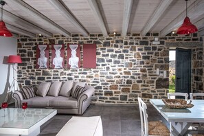 A cozy living room with a stone wall, a sofa, a glass coffee table, and a dining table with chairs.